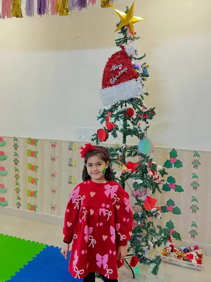 A girl stands proudly in front of the Christmas tree she helped decorate.
