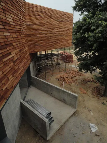 An elevated view of the Rhizome House during construction, showing the application of wooden shingles to the complex, sloping roof forms.