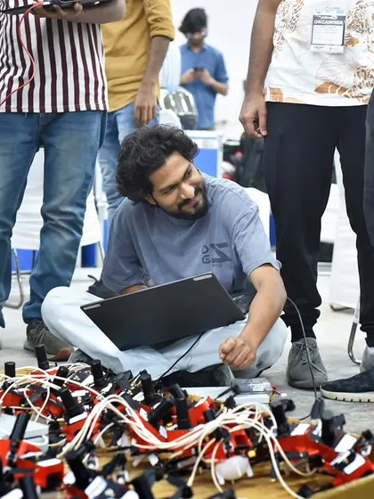 Surrounded by his team and hundreds of drones, our engineer works on his laptop. This image showcases the collaborative spirit and hands-on approach that defines our work ethic.