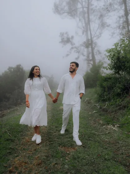 The couple walks hand-in-hand through a foggy forest, creating a magical and atmospheric pre-wedding photograph.