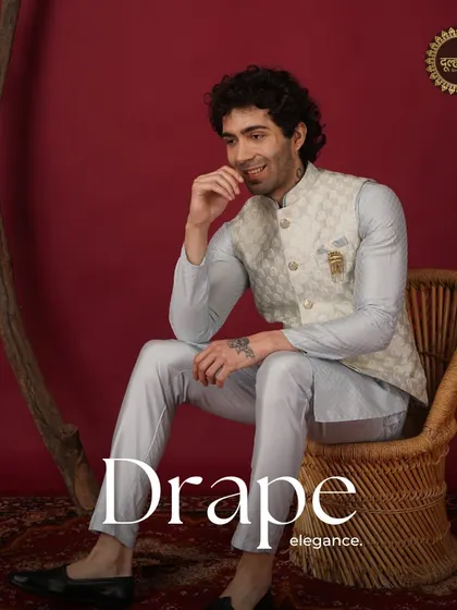 Drape elegance. A model seated in a light blue kurta and beige patterned Nehru jacket, looking relaxed and stylish.