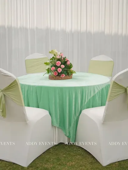 An elegant guest table setup for the Nikah. The pastel green velvet tablecloth is paired with white chair covers and matching green sashes, creating a cohesive and sophisticated look.