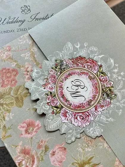 A lovely invitation featuring a die-cut floral monogram. The soft green and pink color palette is modern and refreshing.
