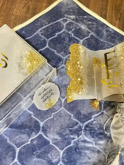 This is the 'Premium Islamic Gift Box for Her'. It includes a personalized grey prayer mat, a luxe Quran holder and box, a crystal tasbih, and a car hanging, all in a beautiful white and gold design.
