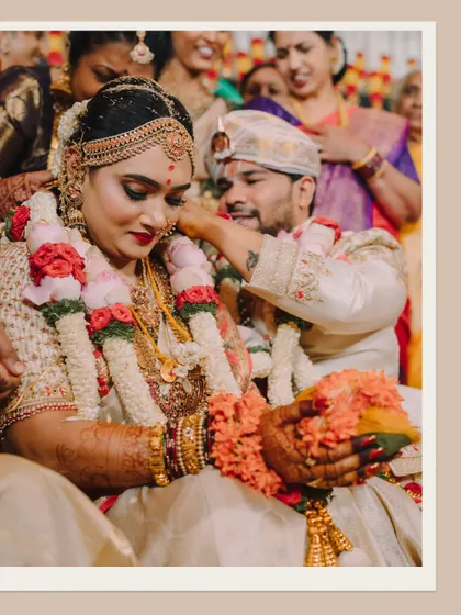 A beautiful moment during the wedding ceremony where the groom adorns the bride. The focus on their hands and the sacred items highlights the ritual's significance.