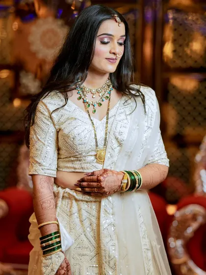A candid portrait of a bride in a beautiful white lehenga, looking down with a soft smile. The focus is on her grace and elegant attire.