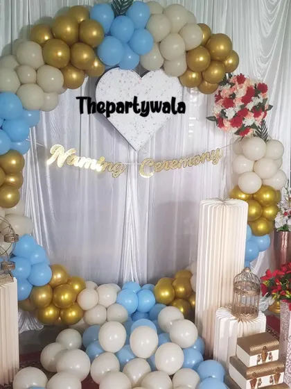 An elegant naming ceremony decoration with a white, blue, and gold balloon arch.