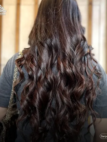 Showcasing voluminous, bouncy curls on long, dark hair. A professional blow-dry and curl service like this can completely transform your look for a day or night out.