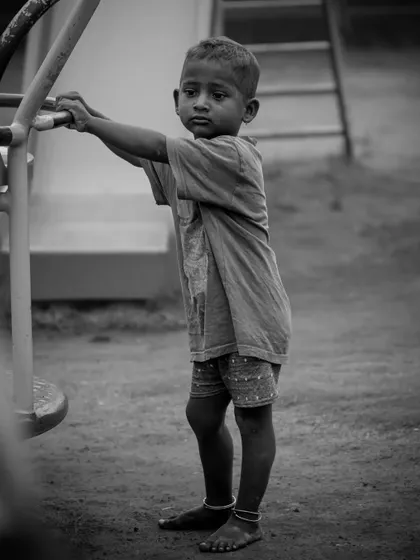 A candid black and white photo of a young boy in a park. The monochrome edit gives the image a timeless feel, focusing on his innocent and slightly sad expression.