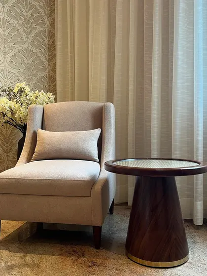 A cozy reading corner in the parent's room. The high-back armchair is paired with a custom-made side table featuring a rattan inlay top and a brass-finished base, continuing the room's theme.