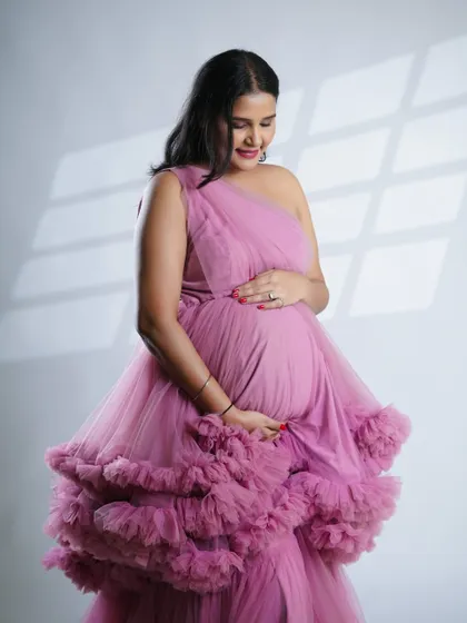 A quiet, reflective moment captured beautifully. The soft light and the gentle hold on her belly convey the deep love and anticipation of motherhood.
