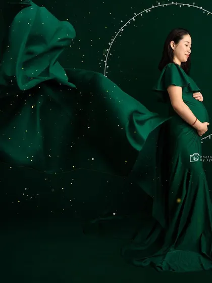 A creative edit of a mom-to-be in a green gown, surrounded by sparkles and a ring of light for a magical effect.