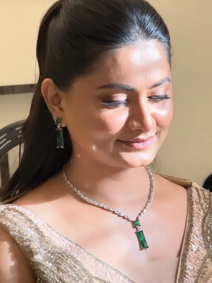 A close-up of a sophisticated engagement look. The makeup is subtle and elegant, with a focus on flawless skin and softly defined eyes, letting the beautiful emerald jewellery stand out.