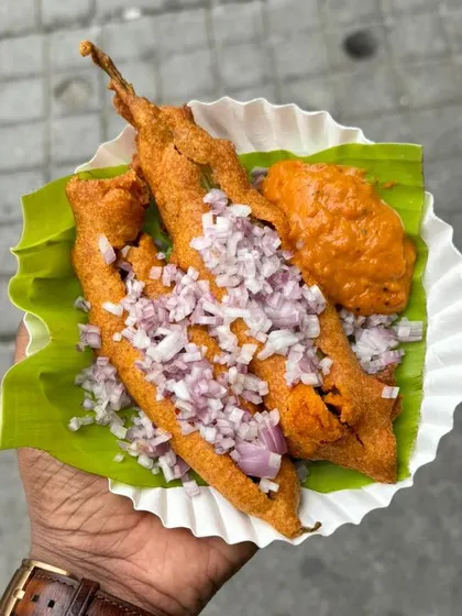 A customer enjoying our crispy Mirchi Bajji, topped with finely chopped onions. It's a perfect spicy snack for a rainy evening.
