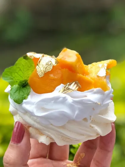 A perfect summer treat. This individual mango pavlova has a crisp meringue shell, fluffy whipped cream, and fresh mango, topped with gold leaf.