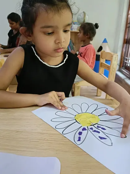 A young girl works on her flower collage, demonstrating her developing fine motor skills. We celebrate the process of creation as much as the final product.