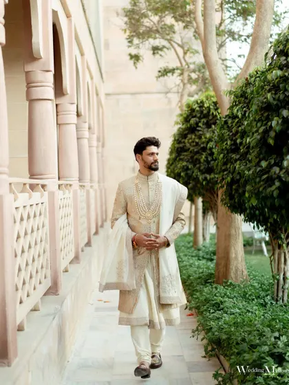 An elegant portrait of the groom, Tejas, looking regal in his wedding attire within the beautiful architecture of the venue.