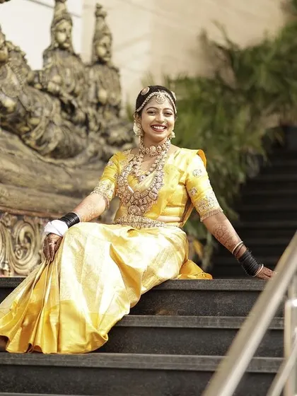 The bride smiling, seated on the steps, looking absolutely radiant on her wedding day.