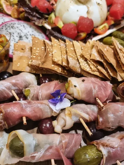 Prosciutto wrapped cornichons sit beside crackers and fruit on our board, a little coldcut bite ready to pick up.