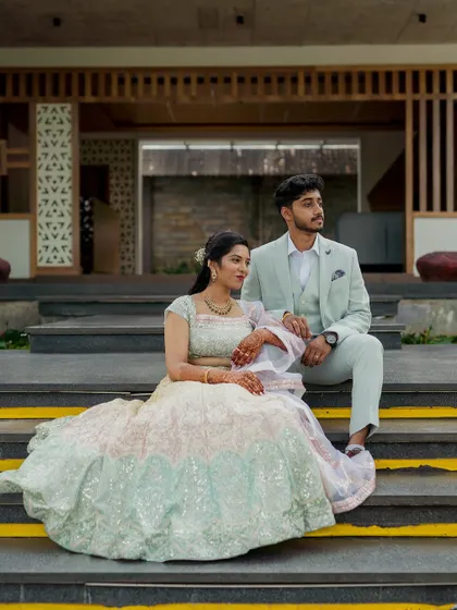 A couple in beautiful pastel outfits, posing on the steps of a modern venue. Their attire perfectly complements the contemporary architecture.