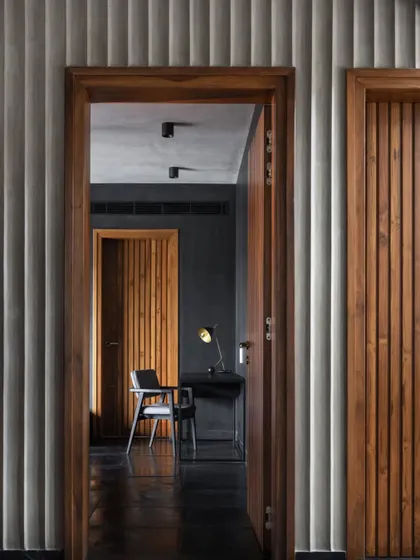 A corridor in the Brick House, where the rhythm of fluted concrete walls and wooden doors creates a visually engaging and layered experience.