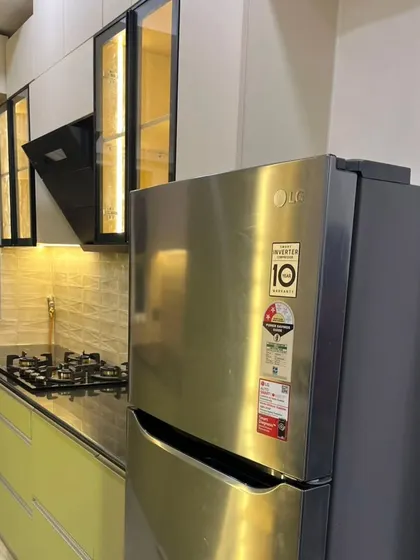 A modern modular kitchen at Mahagun Moderne, Noida. This design features a two-tone color scheme with light green base cabinets and off-white upper cabinets with profile handles.