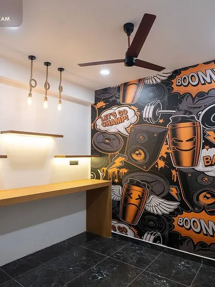 The gym's cafeteria is designed to be a cool-down spot. It features a custom, high-energy graphic wall with comic-book style art, a simple wooden countertop, and warm pendant lighting for a relaxed yet stylish feel.
