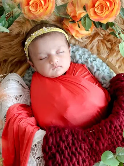 Rich, warm colors make this portrait feel so luxurious. Swaddled in red and deep burgundy, this baby sleeps peacefully among orange roses and eucalyptus leaves.
