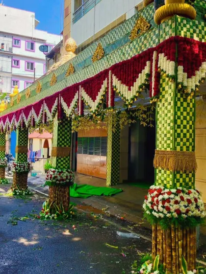 Here is a wide view of a wedding house entrance. I created a large *chappara* with checkered-pattern woven leaves and pillars decorated with sugarcane and fresh flowers.