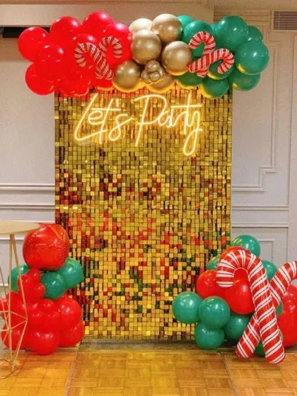 A festive Christmas-themed "Let's Party" backdrop. The gold sequin wall is decorated with red and green balloons and candy cane accents to bring in the holiday cheer.