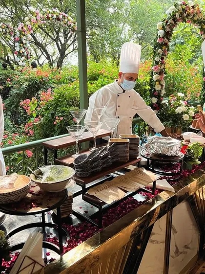 We set up beautiful live cooking stations in any setting, like this outdoor wedding surrounded by lush greenery. Our chefs are seen here preparing gourmet dishes under a floral arch, blending seamlessly with the event's decor.
