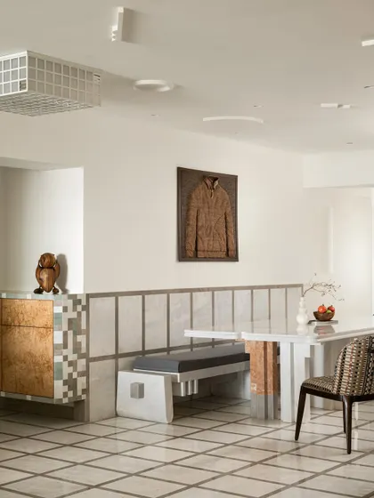 A wider view of the Gingham Dreams dining nook, where a gridded marble floor extends into a dado wall, and a sculpted wooden jacket by Handsminds hangs as art.