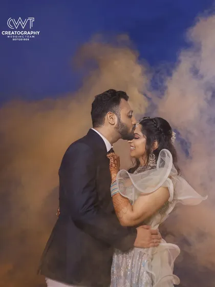 A dramatic and romantic portrait of a couple surrounded by colored smoke, creating a magical atmosphere for their sangeet or reception.