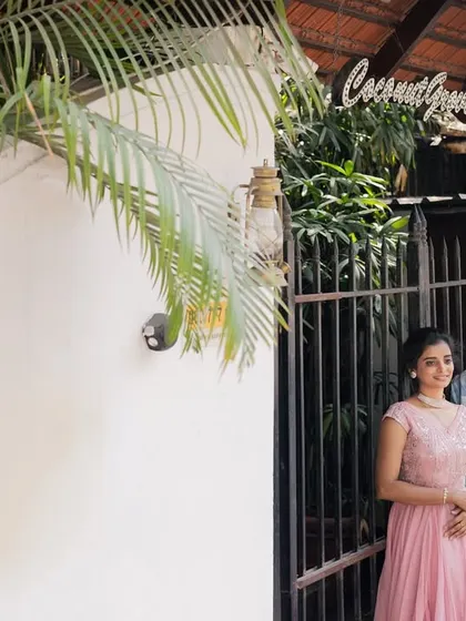 A simple and sweet pre-wedding photo of a couple standing by a rustic white wall and gate, framed by palm leaves.