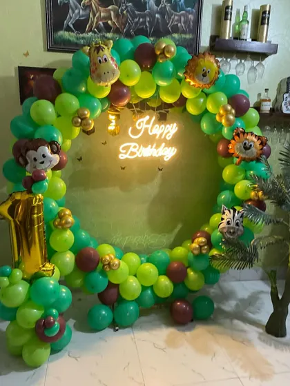 A classic jungle-themed first birthday. This circular balloon arch in shades of green is accented with animal-head foil balloons and a neon 'Happy Birthday' sign.