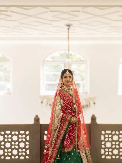 A wide shot showing the bride in a beautiful architectural setting, her red dupatta creating a striking silhouette.