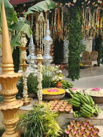 A South Indian wedding setup rich in tradition. The decor features floral gajras, banana bunches, and diyas on banana leaves, with tall golden and silver lamps adding to the sacred ambiance.