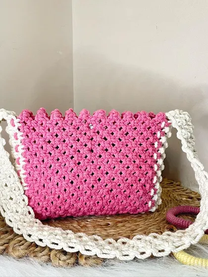 A vibrant pink shoulder bag framed with an off-white border and strap. The scalloped top edge adds a lovely, delicate detail to this eye-catching piece.