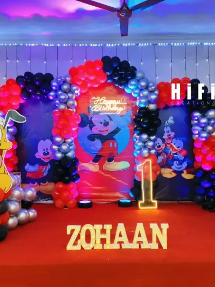 A classic Mickey Mouse Clubhouse birthday party theme. This stage setup features a red, black, and silver balloon arch, character cutouts of Mickey and Pluto, and a personalized backdrop.