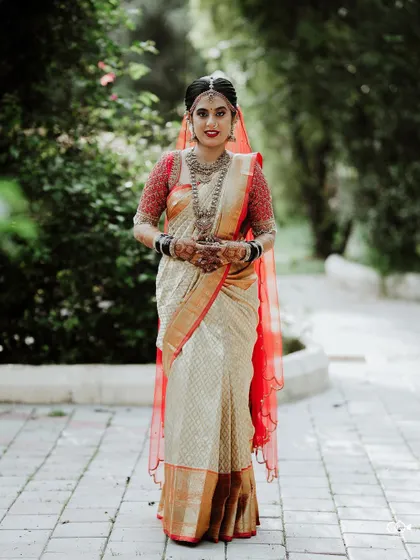 A full-length portrait of the bride in her elegant off-white and red wedding saree.