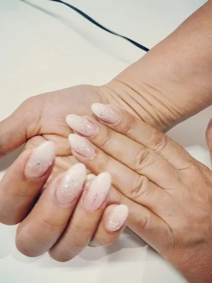A simple and clean look with a soft, shimmery white glitter polish on natural, almond-shaped nails.