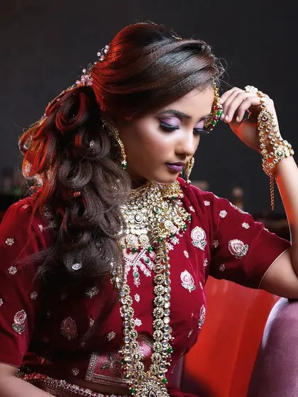 A full view of the royal-inspired reception look. The hairstyle is a voluminous ponytail, which adds a modern touch while keeping the focus on the stunning jewellery and the rich, red outfit.