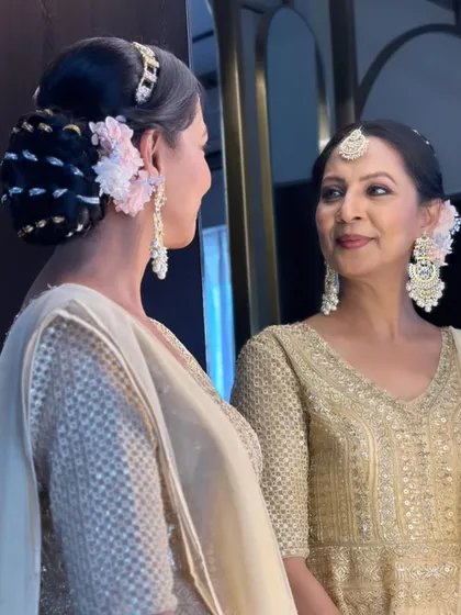 A reflection shot showing both the client and her elegant look in the mirror. The floral bun and soft makeup create a timelessly beautiful style.