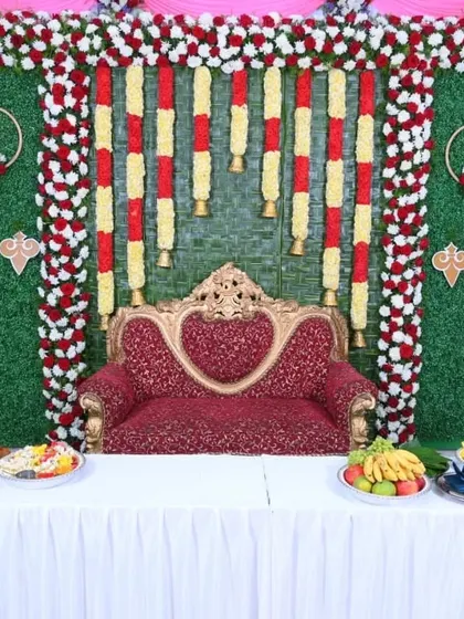 A full view of a traditional baby shower stage. The setup includes the main backdrop, a decorated table for offerings, and a royal red sofa for the parents-to-be.