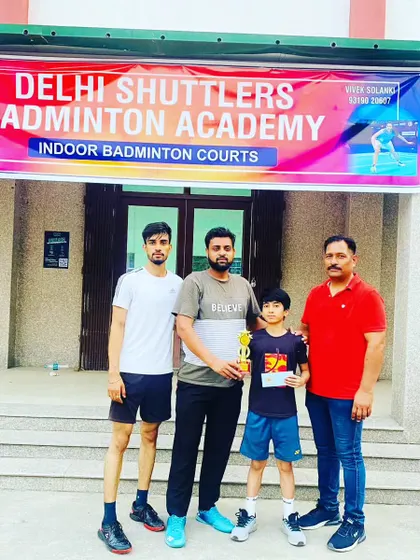 A young champion with his trophy, standing with our coaches in front of the Delhi Shuttlers Badminton Academy banner. We provide end-to-end support for our competitive players.
