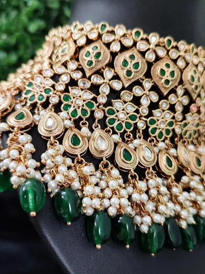 A close-up of a beautiful green choker with floral and leaf motifs. The dangling pearls and green beads add movement and elegance to this rental piece.