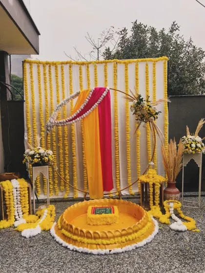 For this Haldi ceremony, I designed a setup that blends tradition with modern elegance. The backdrop features strings of vibrant marigolds, while the seating area is defined by a beautiful urli, all framed by a contemporary golden ring draped in rani pink and yellow fabric.