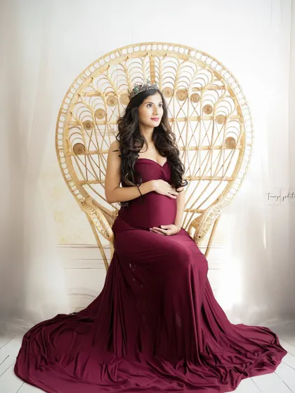 A serene and regal portrait. The mom-to-be is seated on a peacock throne, her expression peaceful and her burgundy gown adding a touch of elegance.