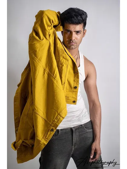 A studio shot of a model holding a yellow denim jacket over his shoulder. This pose creates a dynamic and edgy look, highlighting the jacket as the key piece in this fashion photography session.