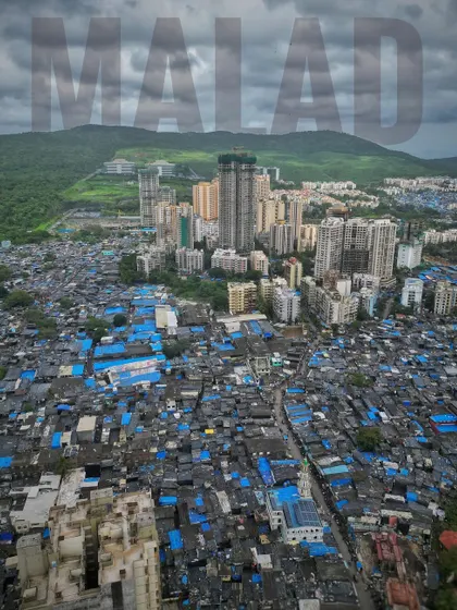 An aerial view over Malad, starkly showing the contrast between the dense, blue-roofed slums and the modern high-rise apartments, with green hills in the background.